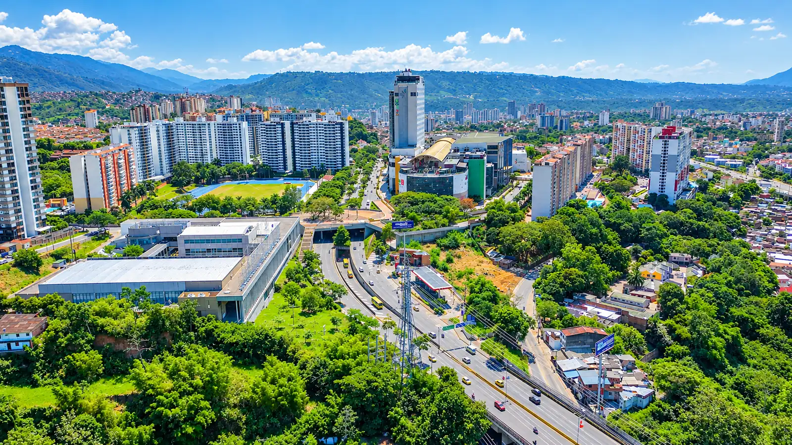 Vista aérea de la ciudad de día con edificios, avenidas, zonas verdes y montañas al fondo